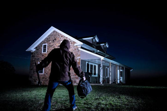 Silhouette of a burglar approaching a well-lit house at night illustrating the psychology of deterrence against break-ins.