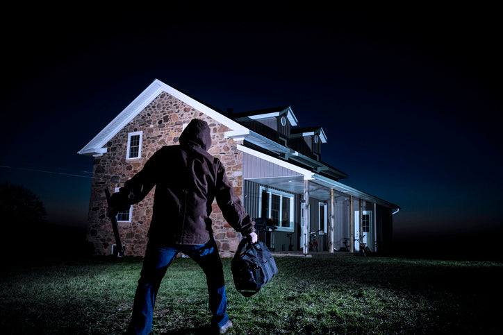 Silhouette of a burglar approaching a well-lit house at night illustrating the psychology of deterrence against break-ins.